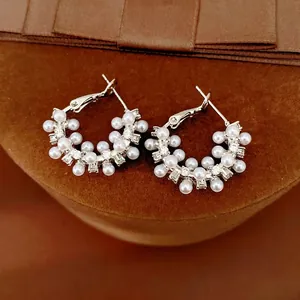 Elegant silver hoop earrings with white pearls and sparkling zirconia on brown velvet.