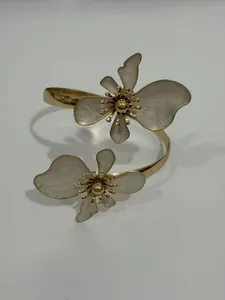 Detailansicht eines goldenen Armreifs mit zwei großen weißen künstlerischen Blumen