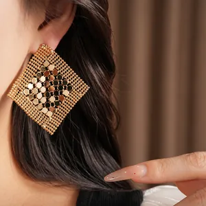 Gros plan d'une boucle d'oreille dorée géométrique en forme de losange ajouré au porté