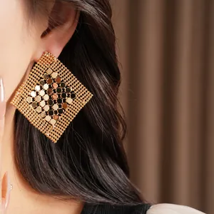 Vue détaillée de grandes boucles d'oreilles géométriques en losange doré sur une oreille