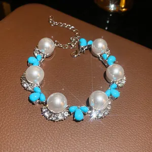 Vista dettagliata di un elegante bracciale con perle bianche, dettagli blu e pietre brillanti.