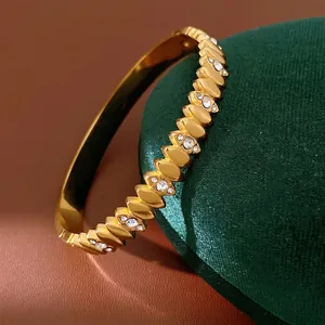 Gold stainless steel bangle bracelet with sparkling zircon inlays on green velvet stand