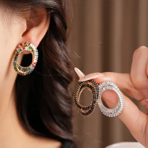 Detail view of luxury zircon elliptical cross earrings in multiple colors worn by model.