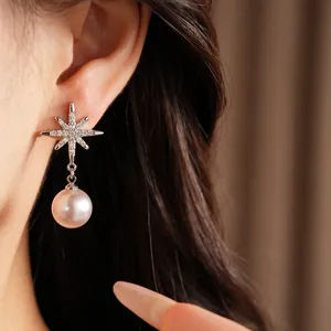 Close-up detail of an elegant zircon star earring with a dangling pearl worn on model's ear