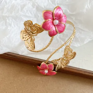 Detailopname van een armband met roze emaille bloemen en gouden vlindermotieven.