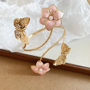 Detailopname van spiraalarmband met roze geëmailleerde bloemen en gouden vlinderhangers