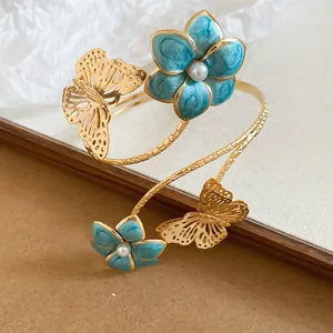 Close-up van de elegante gouden armband met vlinder en blauwe emaille bloemdetails.