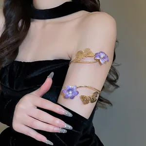 Detail van een bovenarmband met paarse emaille bloem en gouden vlinder voor dames