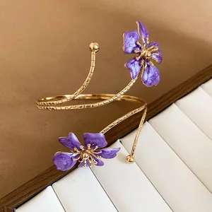 Detail van een gouden bovenarmband met paarse emaille bloemen in een zoete bosstijl