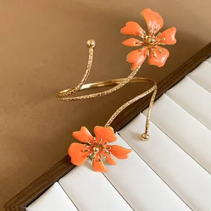 Detailopname van de oranje emaille bloemdetails op een goudkleurige verstelbare armband