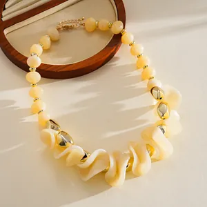 Gros plan d'un collier en acrylique beige épais avec perles ondulées et accents dorés