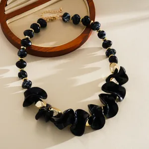 Détail d'un collier en acrylique avec des perles géométriques noires et des reflets dorés.