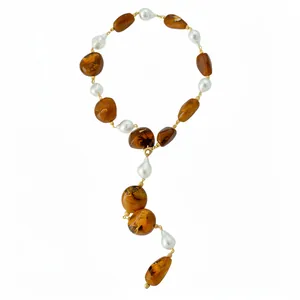 Irregular amber acrylic and white pearl Y-necklace with gold chain on white background.