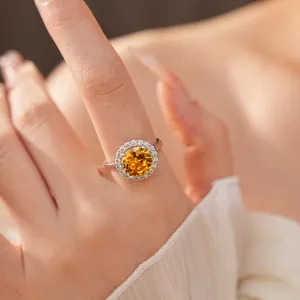 Close-up of elegant silver ring with a round yellow zircon and halo setting on a finger