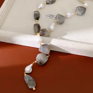 Macro view of irregular grey resin stones and white pearls on a minimalist gold necklace.