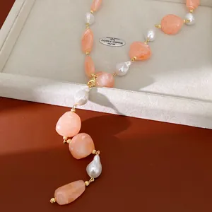 Close-up of irregular peach acrylic beads and white baroque pearls on a gold-toned necklace