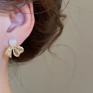 Macro detail of a gold lace bow earring with a white pearl and sparkling zircons.