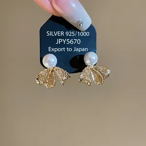 Macro view of elegant 18K gold plated lace bow earrings with lustrous white pearls