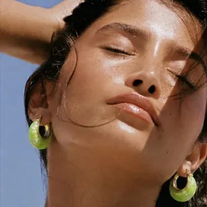 Close-up of model wearing lime green resin hoop earrings with gold accents.