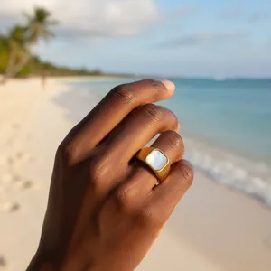 Nahaufnahme eines goldenen geometrischen Muschelrings auf einer Hand am Tropenstrand