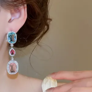 Close-up of elegant drop earrings with light blue, magenta, and pink zircons for evening wear.