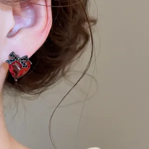 Detail shot of a red heart crystal earring with a black rhinestone bow on a model's ear.