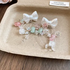 Détail de boucles d'oreilles nœud blanc avec pampilles en cristal coloré sur un plateau