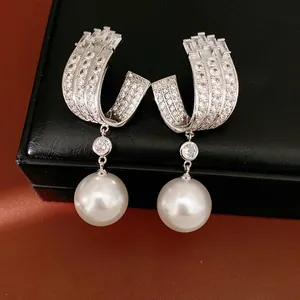 Close-up detail of silver U-shaped earrings with cubic zirconia and pearl drops