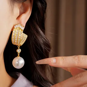 Detailed close-up of luxury gold U-shaped earrings with zircons and large pearl drop