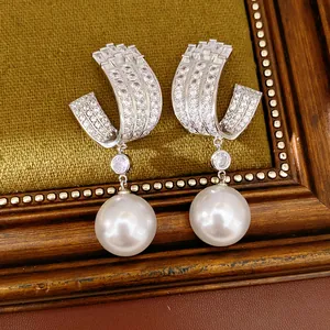 Detailed macro view of U-shaped silver earrings featuring zirconia inlay and large pearls.