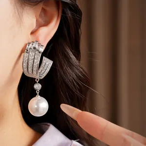 Close-up detail of silver-tone U-shaped earrings with sparkling cubic zirconia and drop pearl
