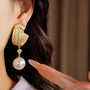 Detail view of a luxury gold U-shape earring with zircons and a large pearl drop