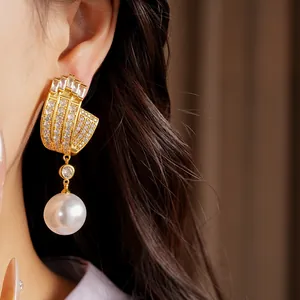 Close-up detail of geometric gold-tone earrings with sparkling zirconia and pearl