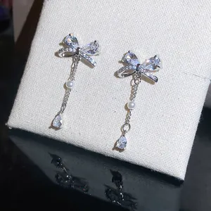 Detailaufnahme von eleganten Zirkon-Schleifen-Ohrringen mit feinen Perlenperlen.