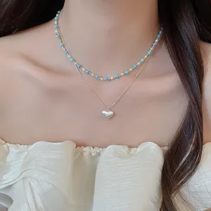 Detailed view of layered necklace with turquoise beads and silver heart pendant on model.