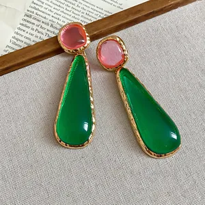 Close-up of vintage artistic earrings with green teardrop and pink irregular resin studs