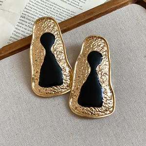 Close-up of vintage geometric gold earrings with hammered texture and black enamel figure.