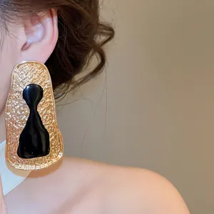 Close-up of retro irregular gold metal earrings with black abstract artistic silhouette