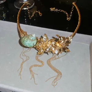 Detail view of a bold gold floral choker featuring a green seashell and long chain tassels