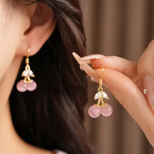 Detail view of pink cat-eye stone cherry earrings with gold plating and zircons