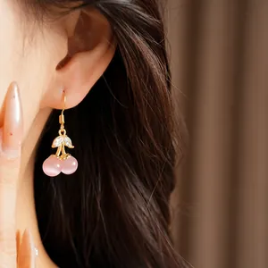 Close-up of pink cat's eye stone cherry earrings with gold plating and zircon leaves
