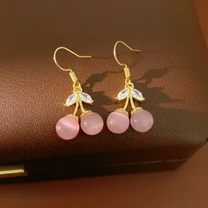 Close-up detail of 18k gold plated pink cat's eye cherry earrings on leather box