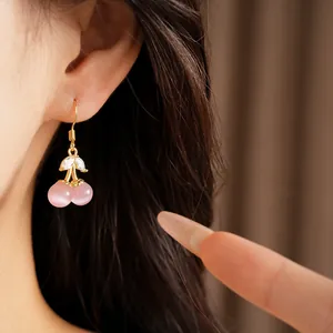 Close-up of 18k gold plated cherry drop earrings with cat's eye stone on model