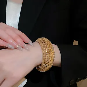 Detailaufnahme einer goldfarbenen, perlenbesetzten, offenen Manschettenarmspange am Handgelenk