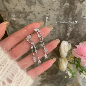 Close-up of sparkling cubic zirconia heart and waterdrop tassel earrings held by a hand
