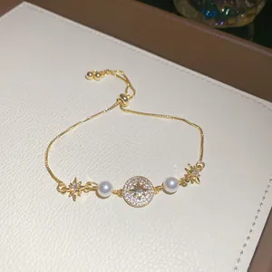Dettaglio di un braccialetto dorato con pavé di zirconi, perle bianche e ciondoli a stella