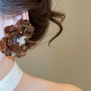Close-up view of a large brown acrylic flower earring with clear crystals on a model's ear