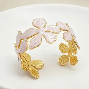 Dettaglio di un bracciale rigido in acciaio dorato con fiori a cinque petali in smalto rosa