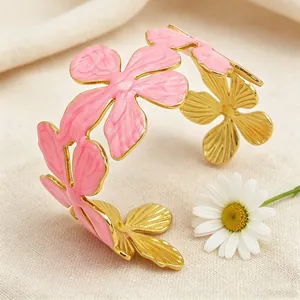 Dettaglio ravvicinato del fiore di smalto rosa sul bracciale rigido dorato ed elegante