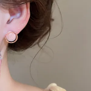 Primer plano de un elegante pendiente rosa ojo de gato con marco de oro rosa en la oreja.